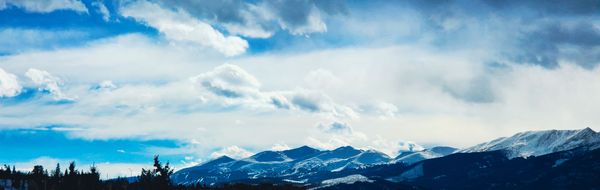 Panoramic view of snow-capped mountains under a vibrant blue sky with dramatic white clouds