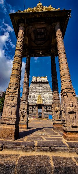 Grand ancient stone gateway with carved pillars frames an intricate white temple tower under a vibrant blue sky