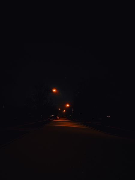 A dark, empty street at night with orange streetlights casting a warm glow on the asphalt