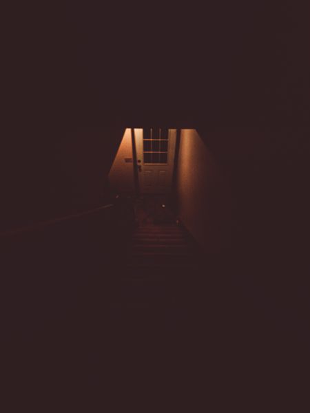 A dimly lit staircase ascends towards a white door with windows, illuminated by a warm, inviting light