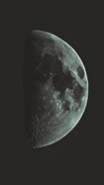 A detailed portrait view of a half-illuminated moon, showcasing its rugged, cratered surface against the dark expanse of space
