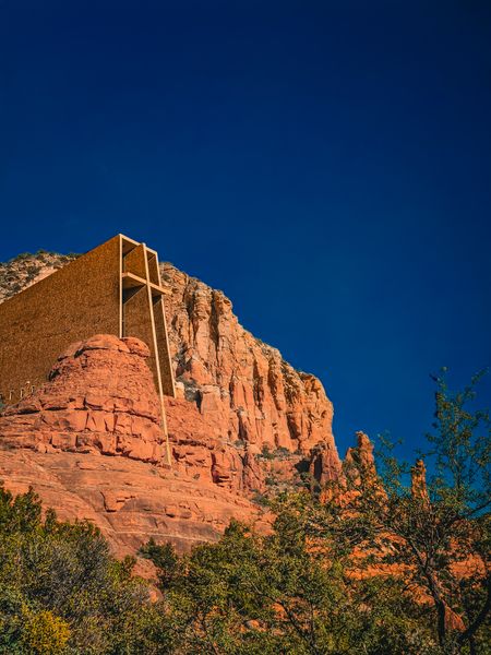 A modern chapel with a prominent cross embedded in vibrant red cliffs against a deep blue sky