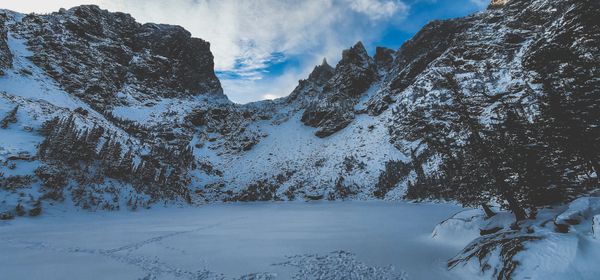 Panoramic view of a frozen lake and snow-covered mountains under a vibrant blue sky with clouds
