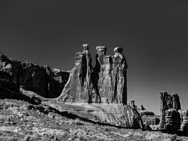 Striking black and white landscape showing three towering sandstone rock formations under a clear desert sky