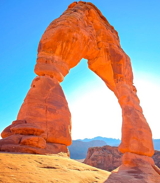 A towering, bright orange sandstone arch, Delicate Arch, stands against a vibrant blue sky in a desert landscape