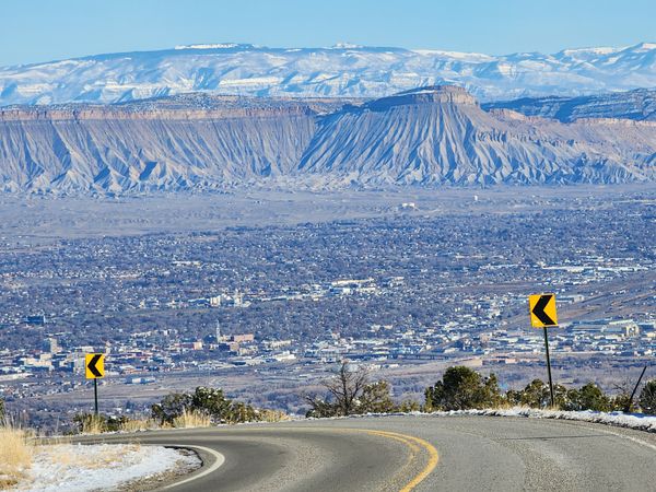 Winding road overlooking a sprawling city with dramatic flat-top mountains and snow-capped peaks in the distance