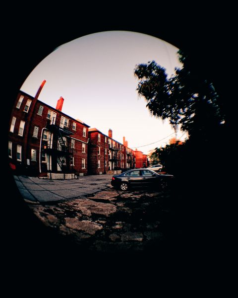 Distorted fisheye view of old brick buildings with fire escapes, a parked car, and a tree silhouette