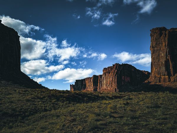 Dramatic desert landscape featuring towering red rock formations under a vivid blue sky with scattered white clouds