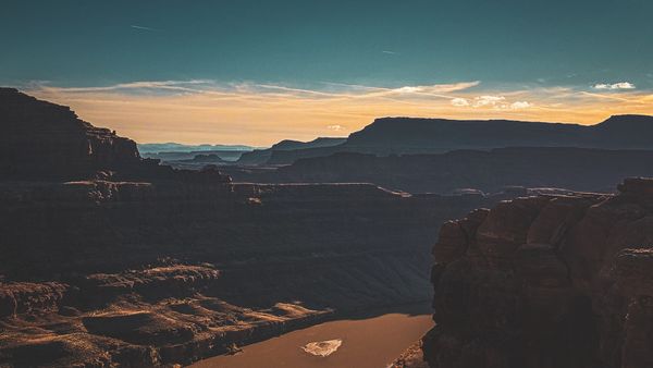 A grand canyon landscape at sunset, featuring a winding river and vast layered rock formations under a vibrant sky
