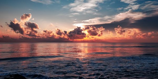 Dramatic sunset over the ocean, with vibrant orange and pink clouds reflecting on the calm water