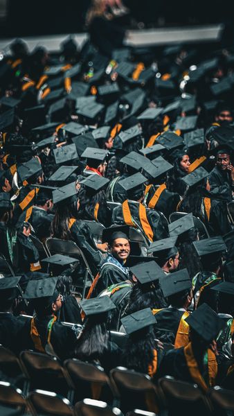 Smiling graduate in cap and gown among a crowd of other graduates at a ceremony